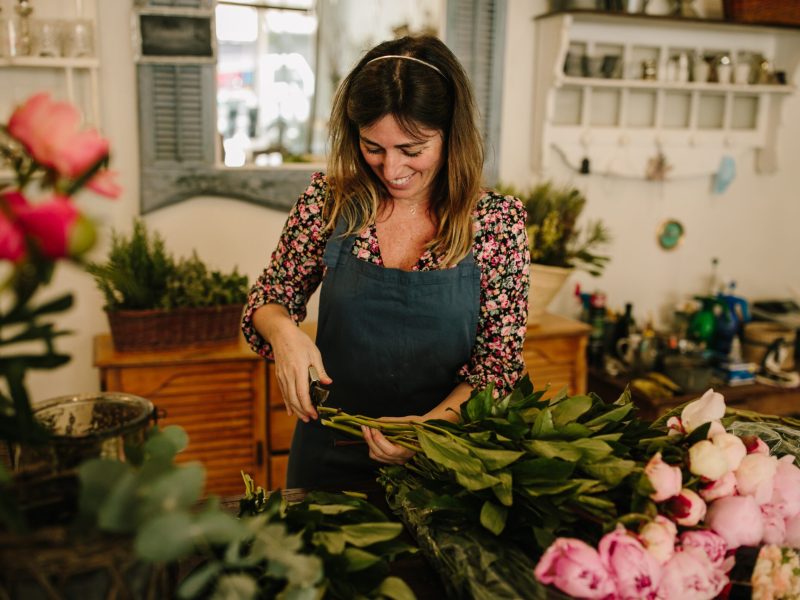 A European female florist with a green apron making flower arrangements in a floral design studio
